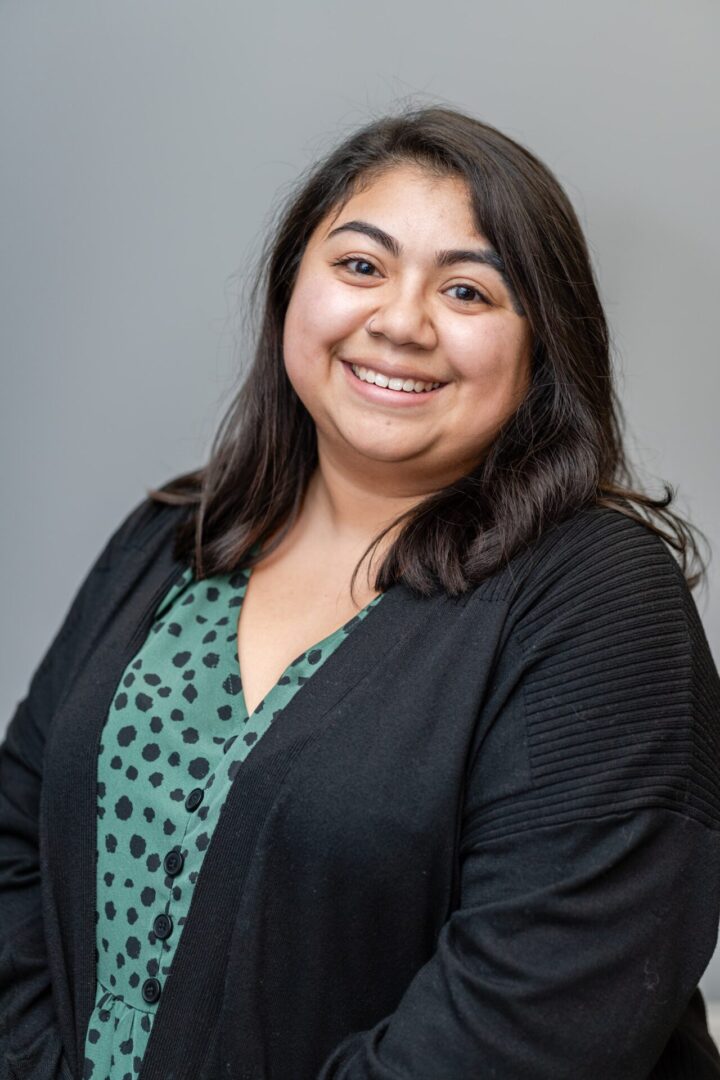 A woman in black jacket and green shirt smiling.