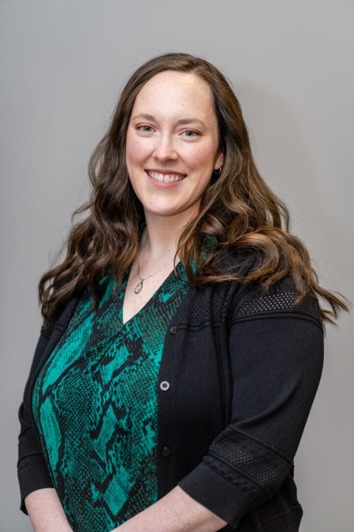 A woman in black jacket and green shirt smiling.