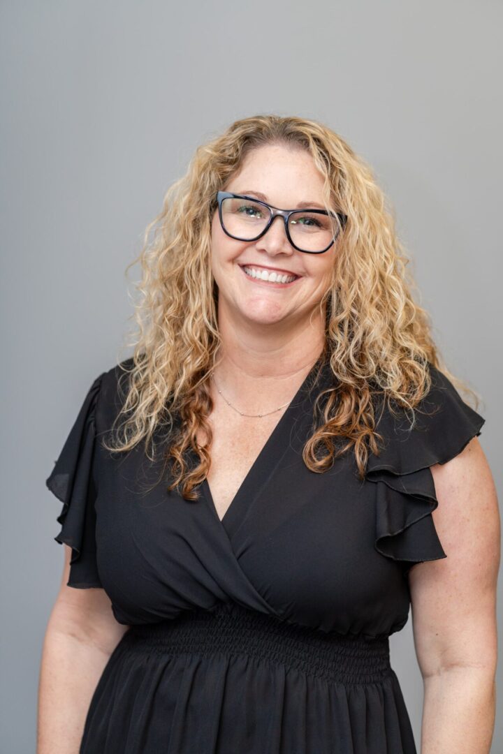 A woman with curly hair wearing glasses and black shirt.