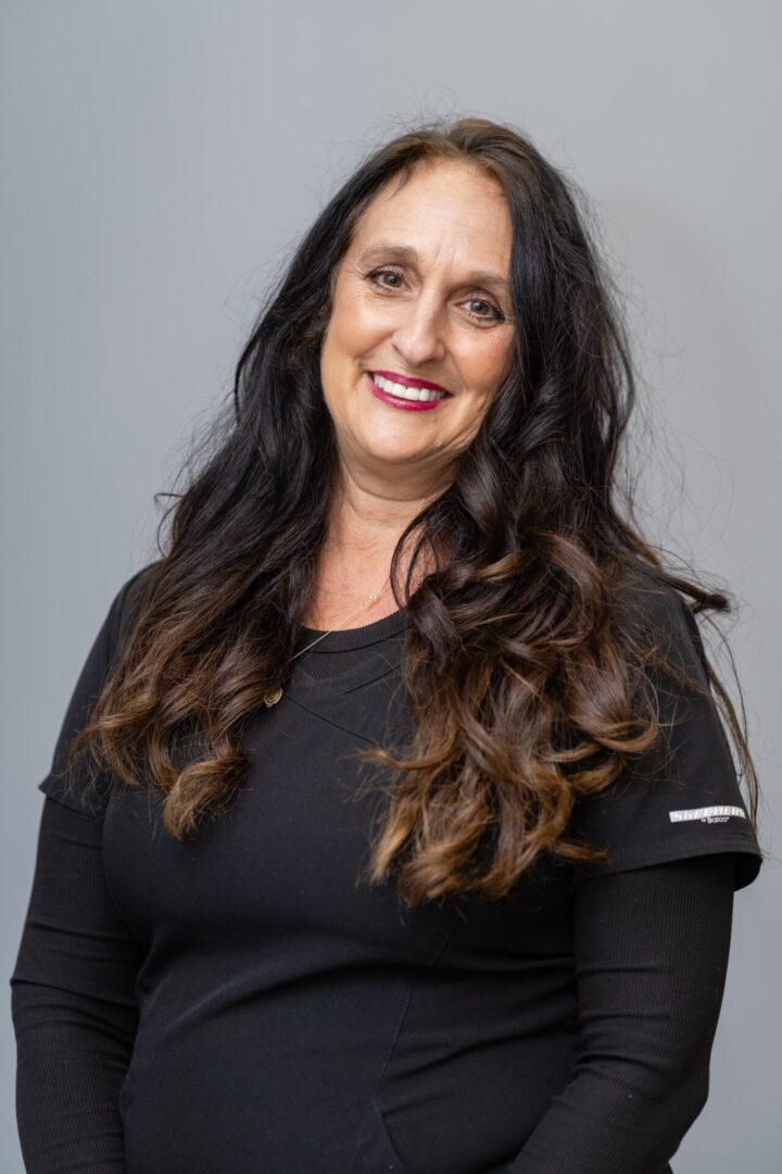 A woman with long hair and wearing black is smiling.